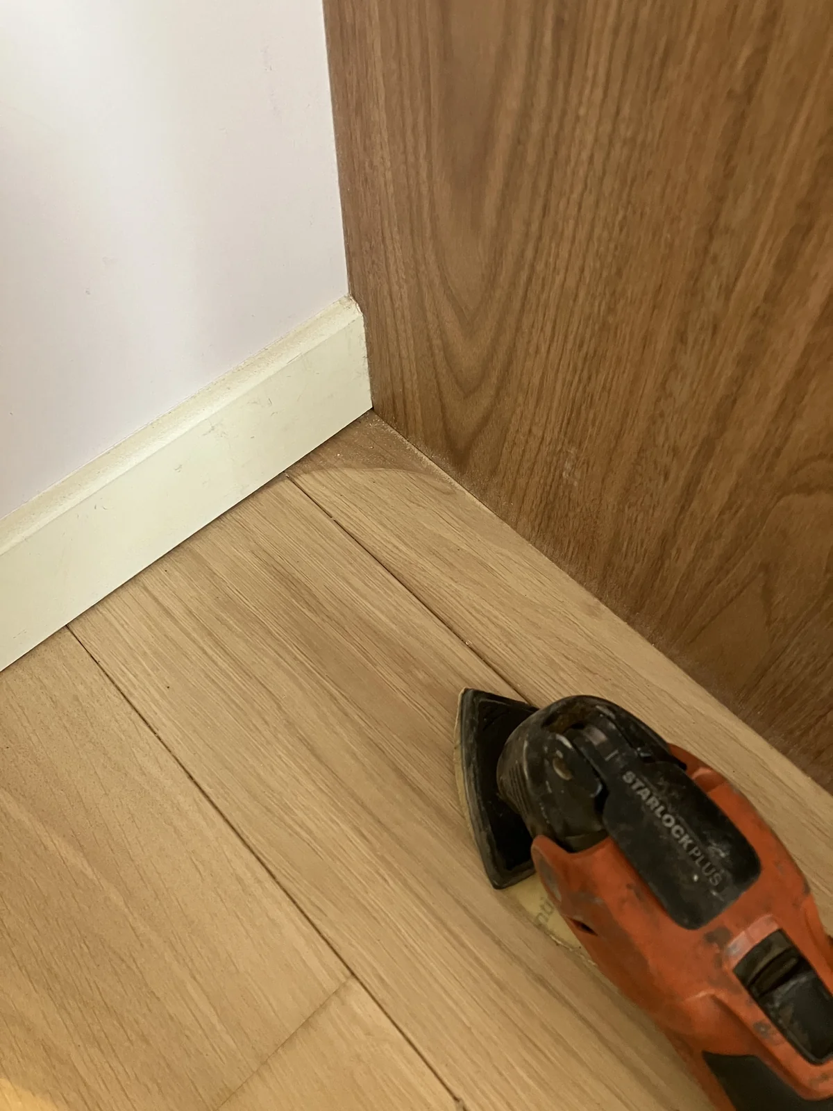 Ponceuse oscillante à plateau delta poncant l'angle d'un parquet contre une plinthe et un panneau bois