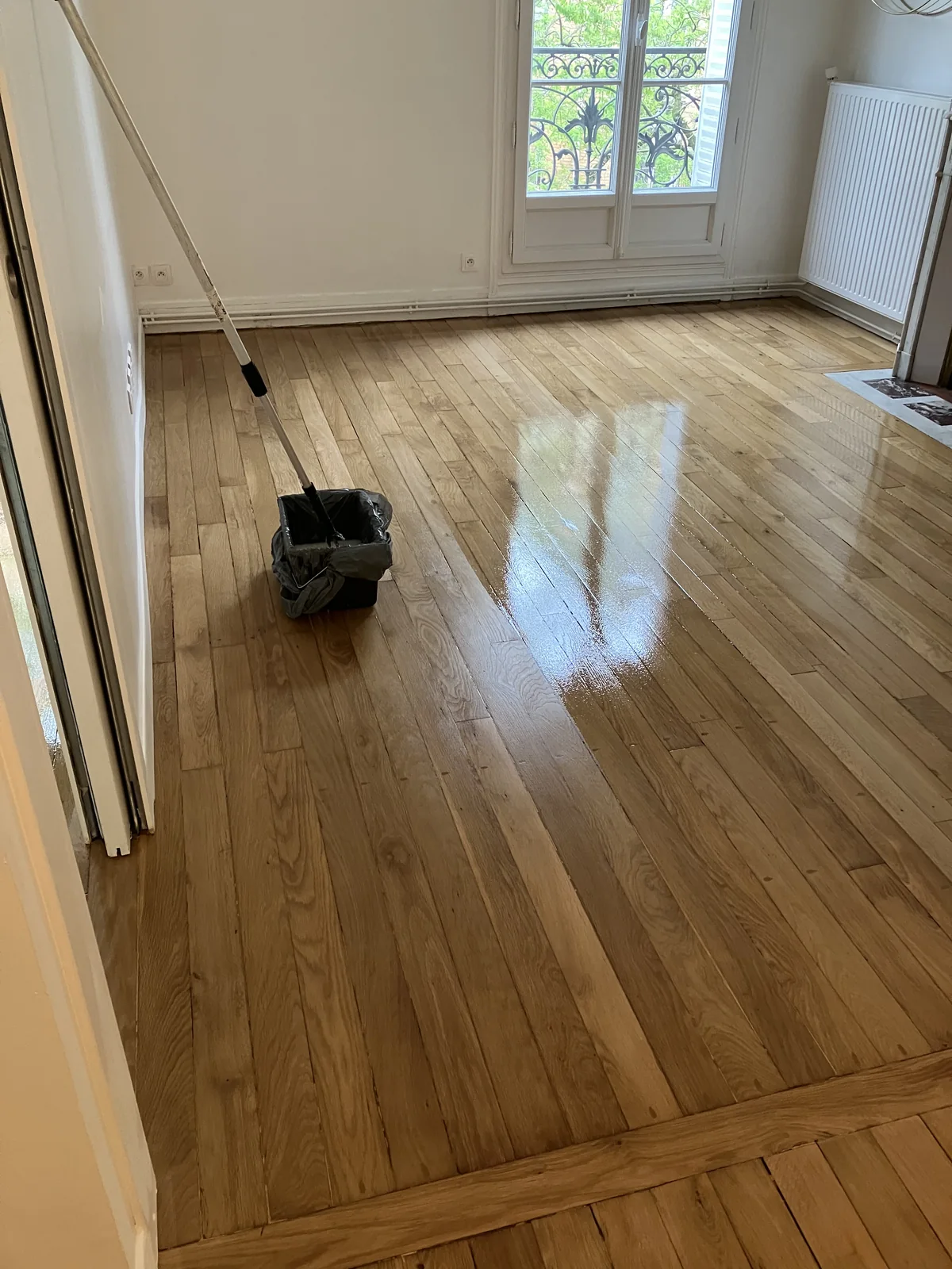 Trois couches de Bona Mega Evo, égrenage entre la première et la deuxième. Le chêne massif haussmannien a retrouvé sa couleur naturelle — le vernis à base aqueuse ne jaunit pas. Comparez avec la première photo&nbsp;: c'est le même parquet, le même bois, la même pièce.