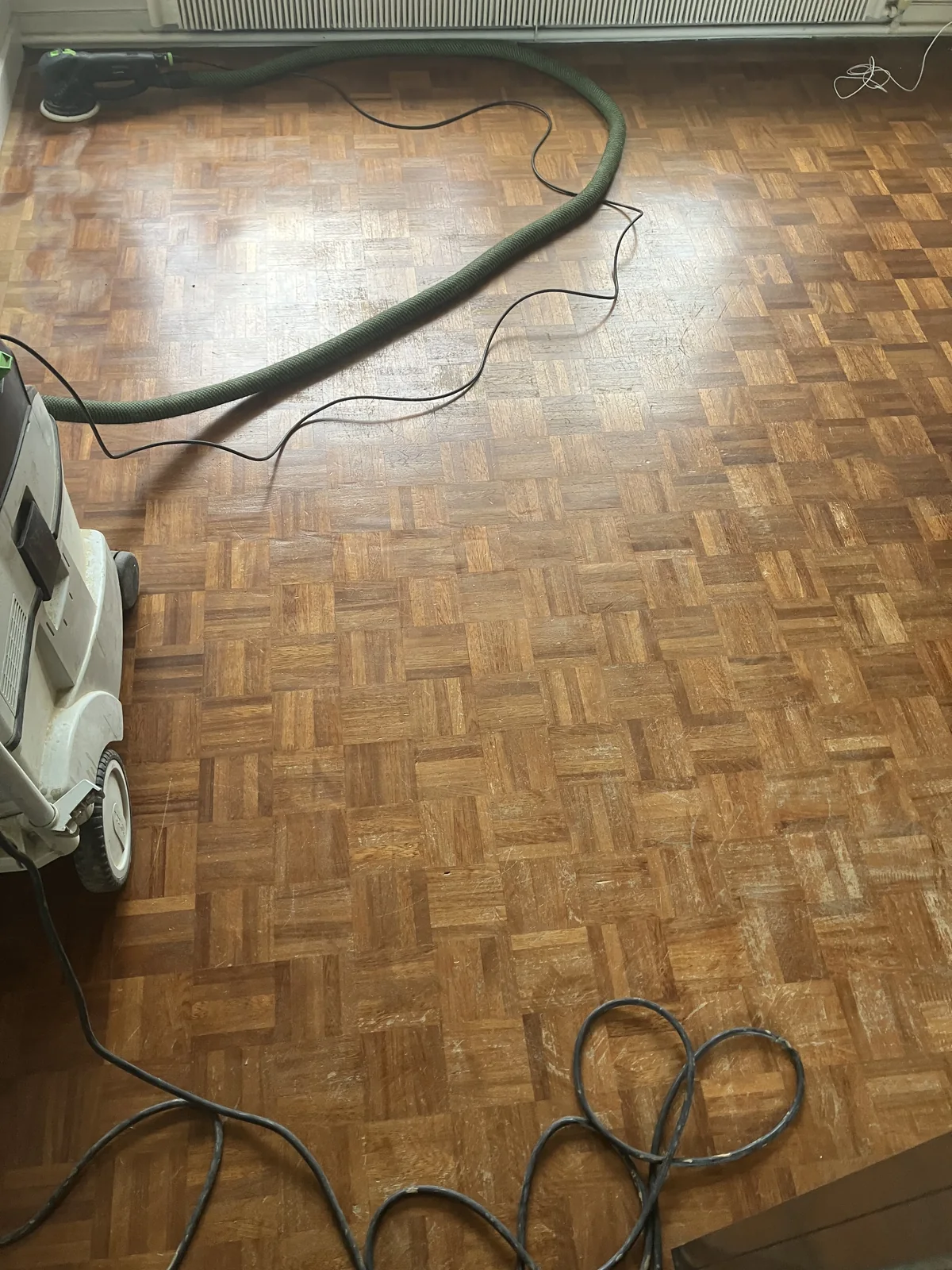 Un parquet mosaïque recouvert d'un vernis ancien brun-acajou : terni, rayé, la teinte assombrissait toute