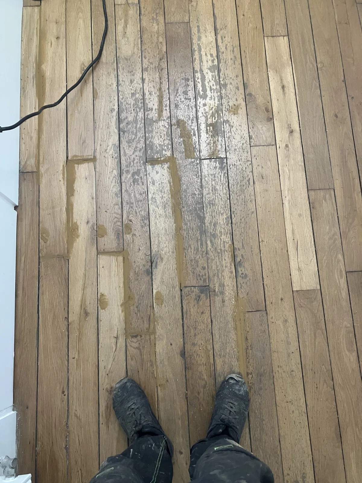 Trous de clous, éclats et traces d'un ancien revêtement collé, rebouchés à la pâte à bois avant le ponçage. Paris 17e.