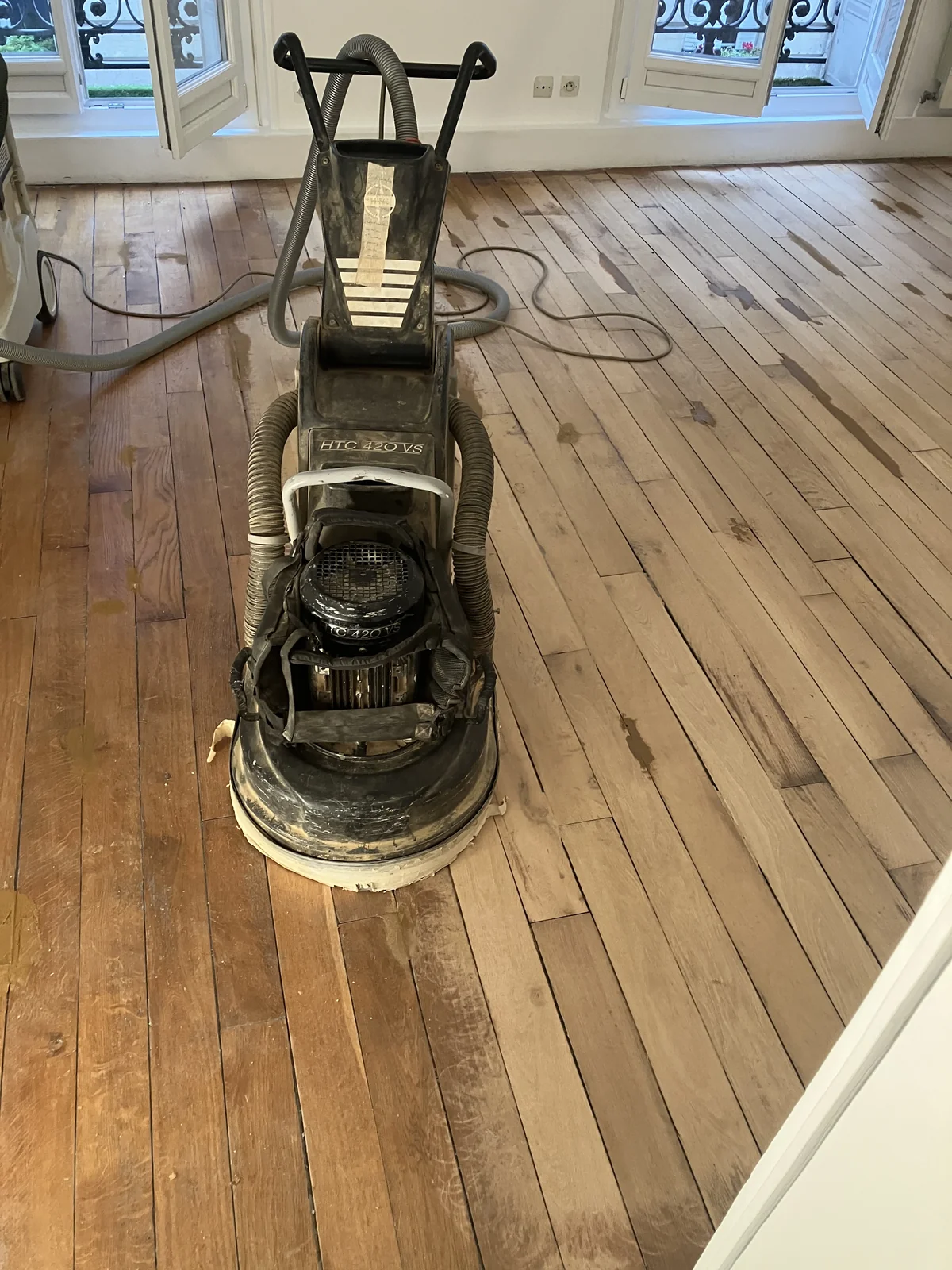 La machine planétaire sur un parquet en chêne à lames droites. Aspiration branchée en permanence, fenêtres et balcon parisiens en arrière-plan.