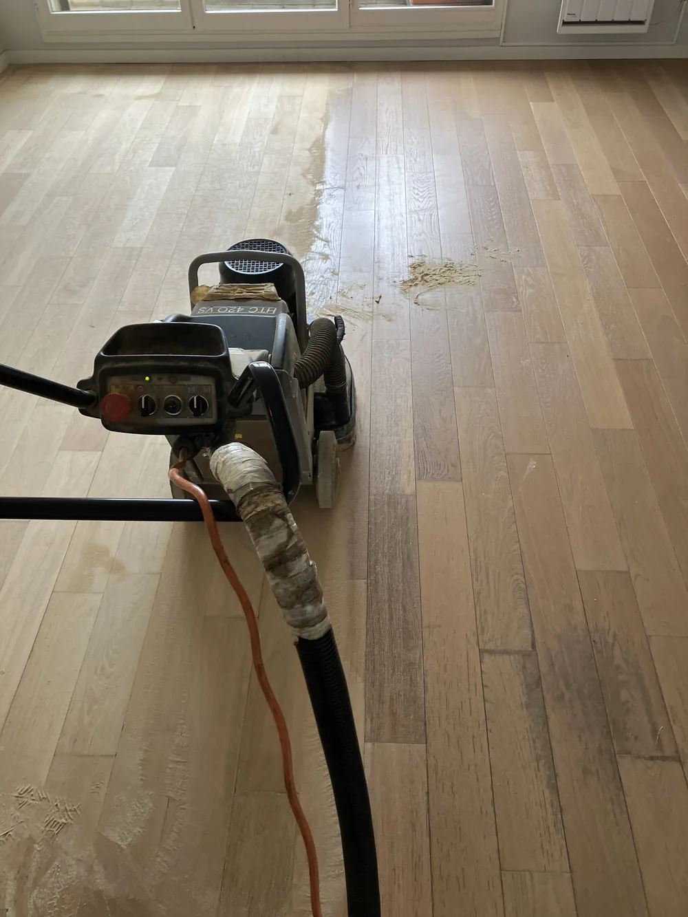 À droite, le parquet tel qu'il était&nbsp;: vernis usé, teinte foncée, taches. À gauche, le même bois après un seul passage de la machine. Cette ligne de séparation, c'est tout le métier en une image.