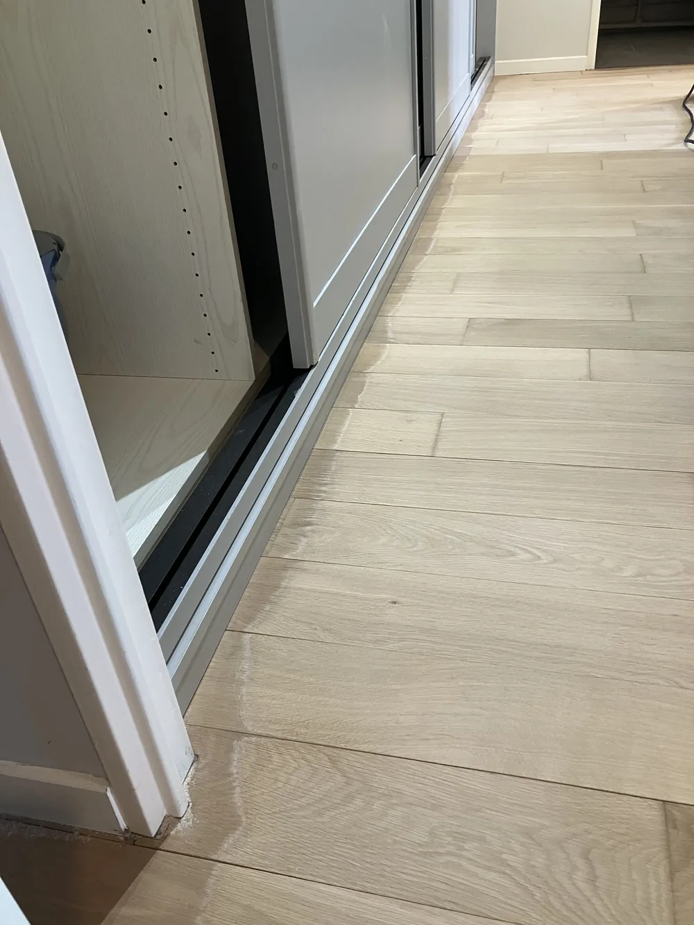 Le parquet est poncé au ras du rail du placard coulissant. On ne laisse pas de bande sombre le long des seuils.