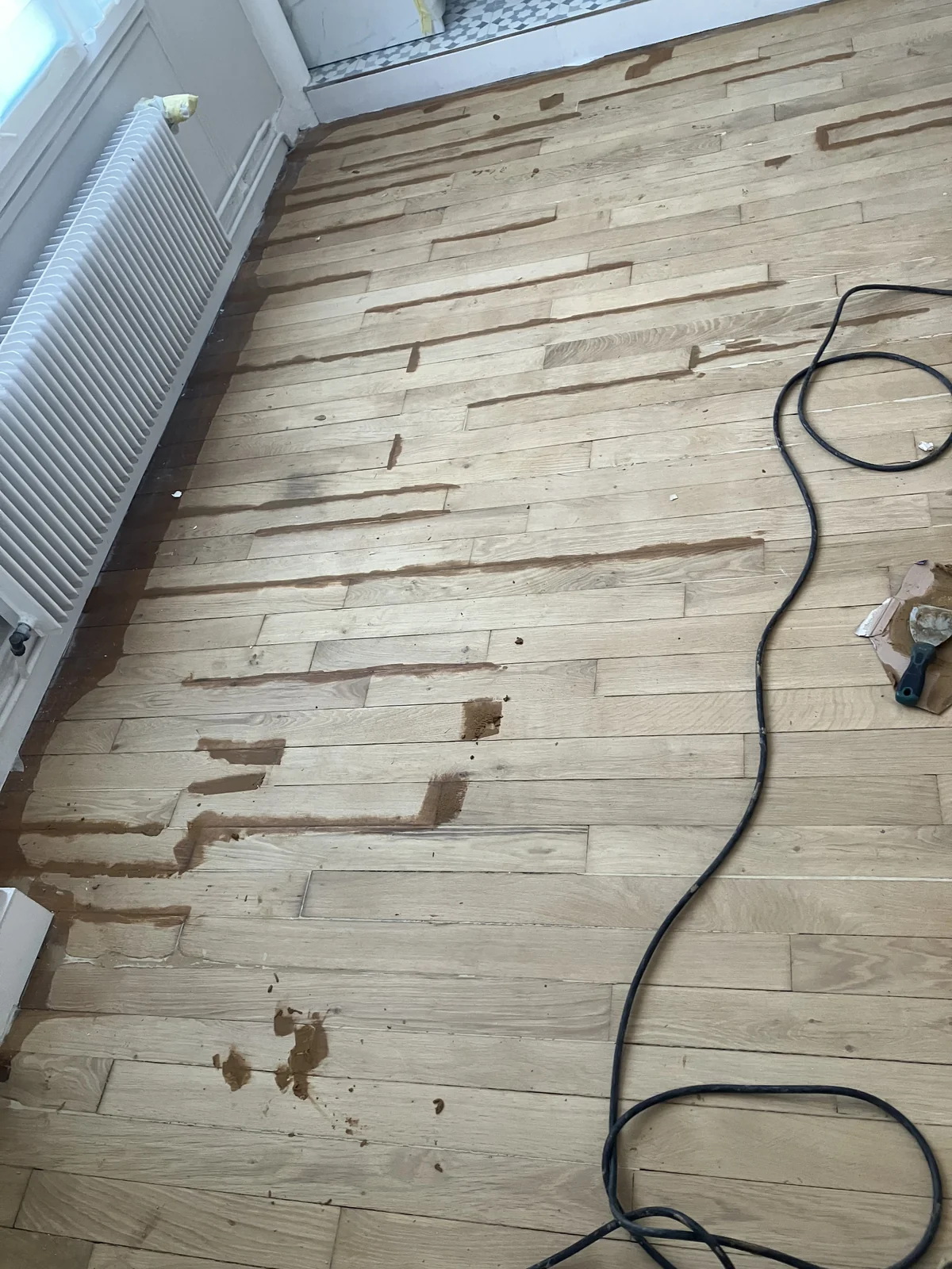 Rebouchage des joints entre les lames à la pâte à bois sur un parquet en chêne poncé — chantier Paris 16e