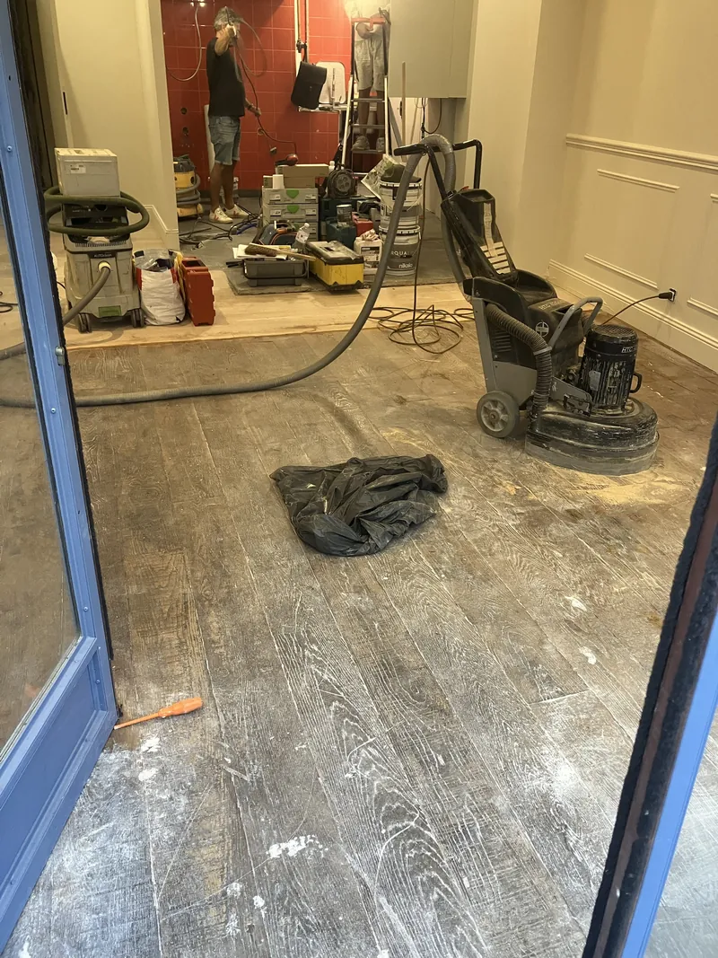 Parquet chêne usé et taché d'une crêperie rue de l'Arbre Sec, Paris 1er, avant ponçage — machine planétaire HTC en place