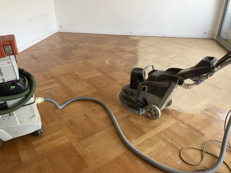 Ponçage en cours d'un parquet mosaïque en chêne à Montsouris, Paris 13e — machine planétaire HTC, moitié vernie ancienne, moitié poncée