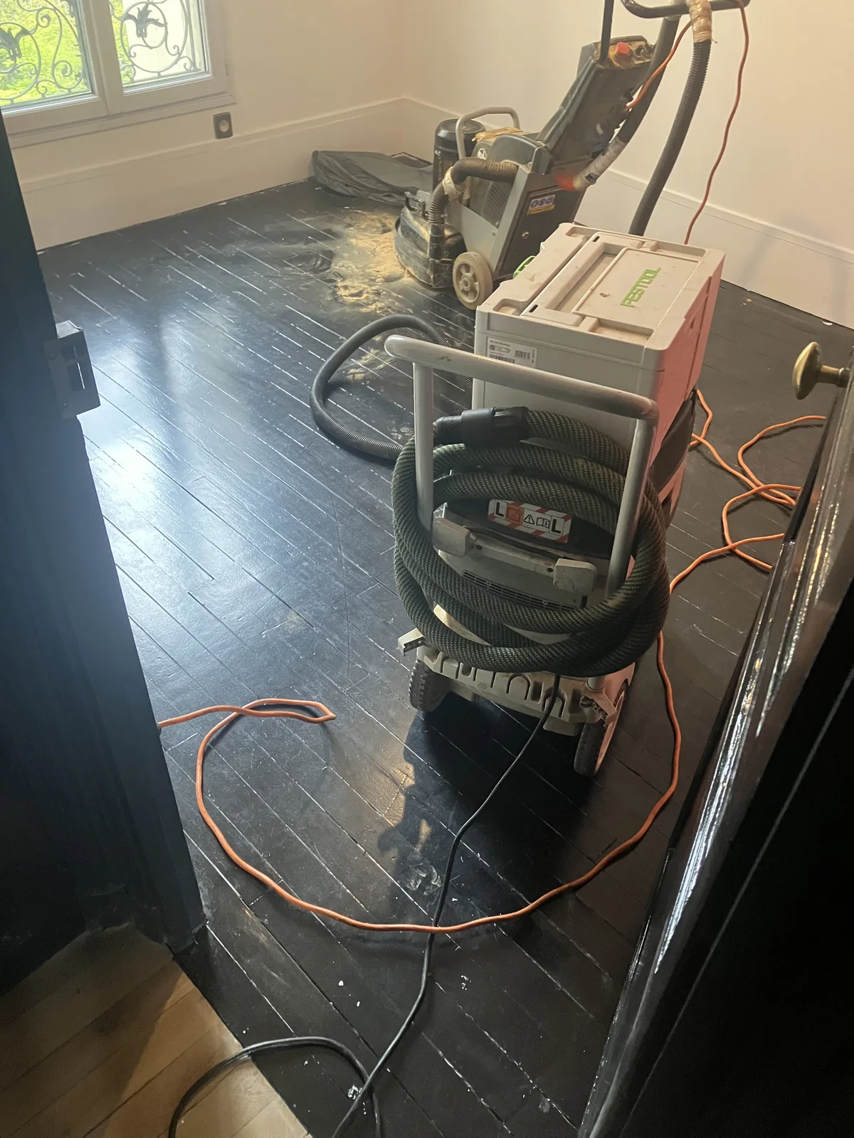 Parquet en chêne peint en noir en cours de décapage à la machine planétaire — rue de Vouillé, Paris 15e
