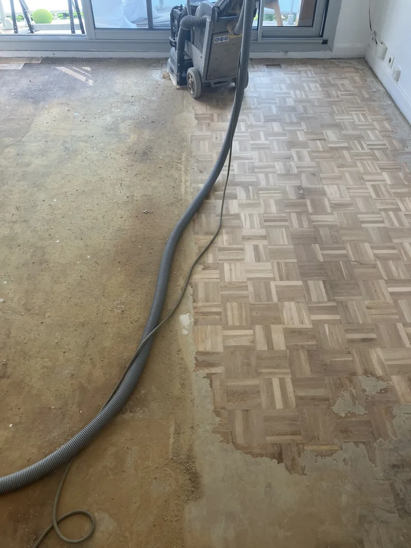 En cours de ponçage — parquet Versailles avec résidus de colle à gauche, zone poncée propre à droite