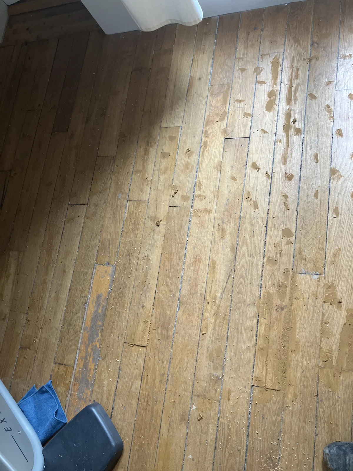 Rebouchage localisé à la pâte à bois : trous de clous et éclats repris un par un sur un parquet en chêne